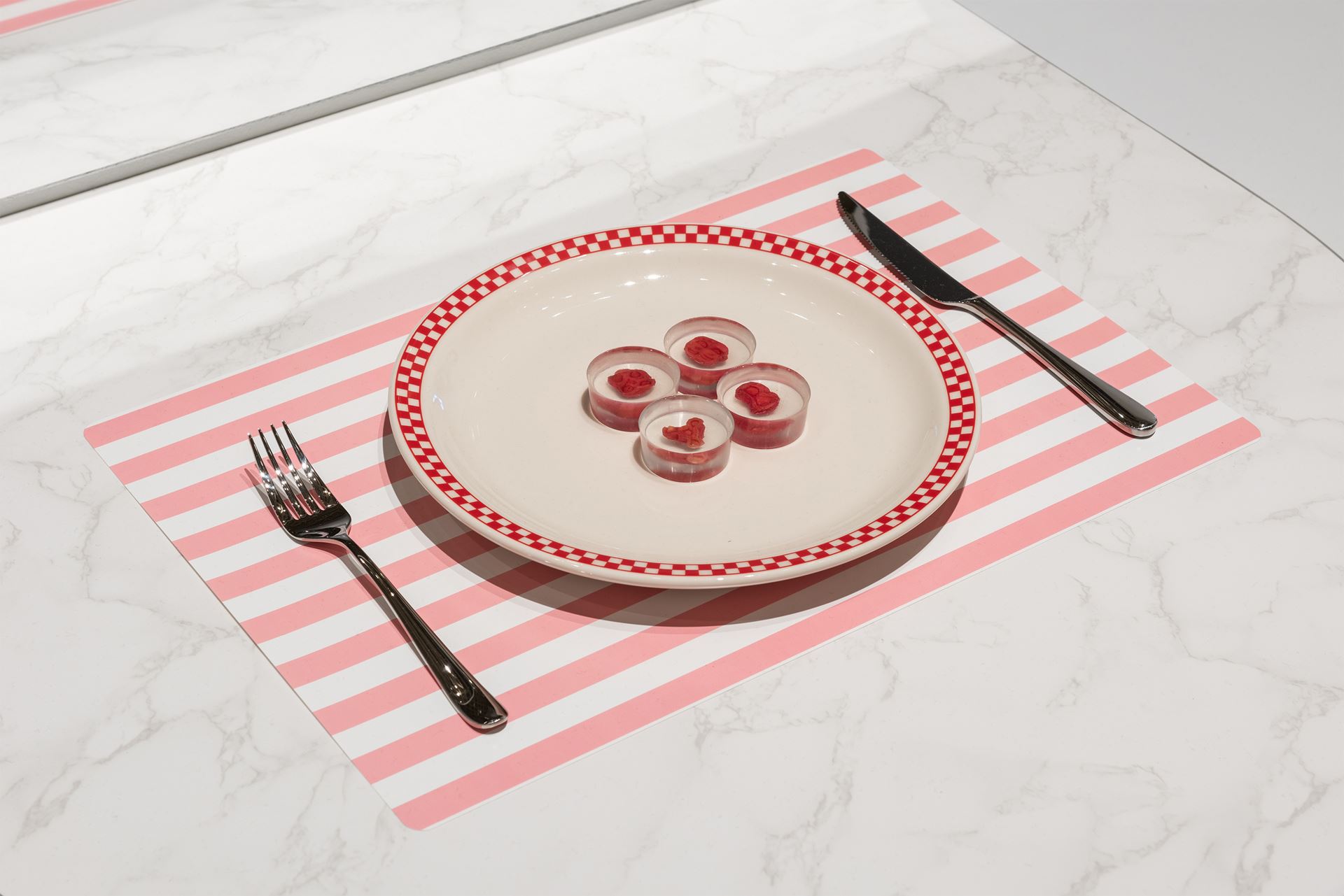 Four steaks preserved in tea-light size resin cylinders placed artfully in the centre of a plate, with knife and fork to the side, as if ready to be eaten.